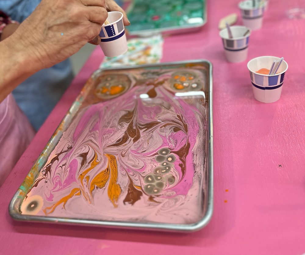 Hands adding paint to a marbling tray during a leather marbling workshop